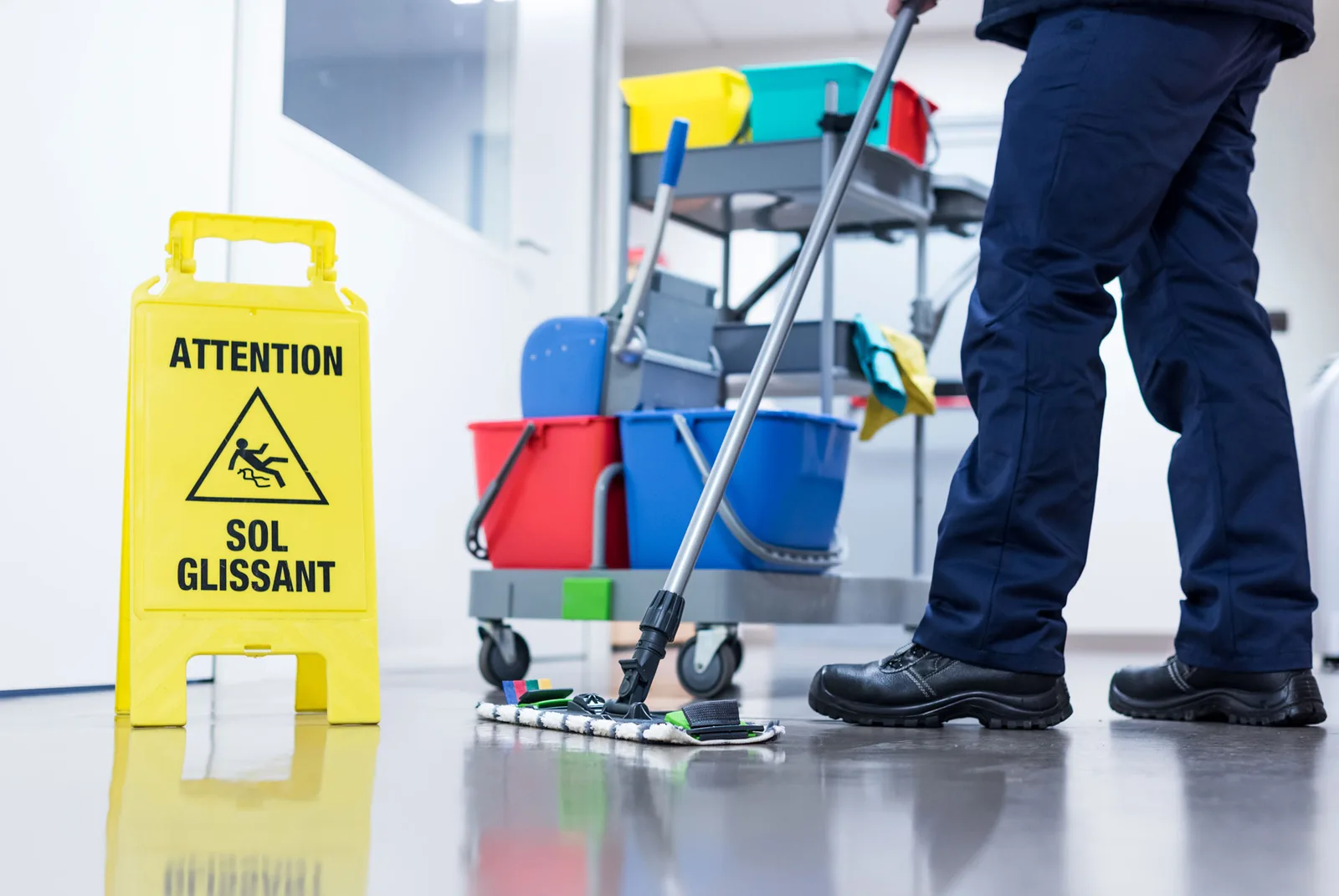 Reinigungskraft wischt einen Hartboden, daneben ein Reinigungswagen